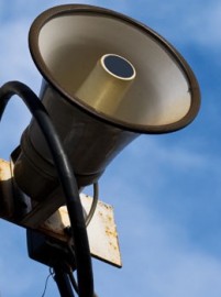 Industrial warning siren on a post against theblue sky.